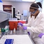 A scientist pipetting a solution into a container in a laboratory setting.