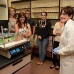A group of students with a lab technician observing equipment in a science laboratory.