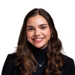 A young woman with long brown hair, wearing a black blazer and turtleneck, smiles at the camera against a white background.