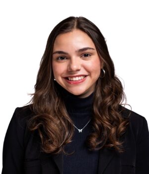 A young woman with long brown hair, wearing a black blazer and turtleneck, smiles at the camera against a white background.